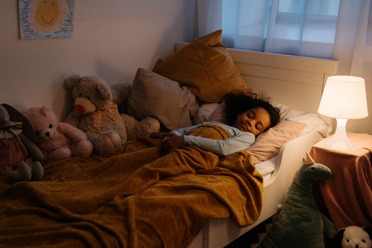 A young girl sleeping peacefully in a cozy bed surrounded by stuffed animals under a warm nightlight, illustrating why quality sleep is essential for child growth and development